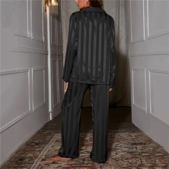 Frau in schwarzem gestreiftem Satin-Pyjama im Flur, elegante Nachtwäsche, gemütlich.