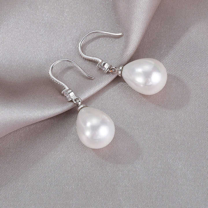 Silberne Ohrringe mit weißen Perlen, elegantes Schmuckdesign auf grauem Stoff.
