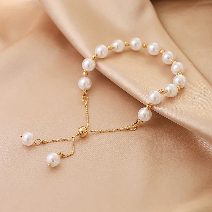 Goldenes Armband mit weißen Perlen auf beigem Stoff, eleganter Schmuck, Damenaccessoire.