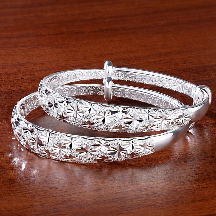 Silberne Armreifen mit Sternmuster auf Holzoberfläche, eleganter Schmuck, Damenaccessoire.