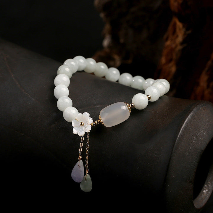 Jade-Armband mit weißen Perlen, Blumenanhänger und goldenen Akzenten auf schwarzem Hintergrund.
