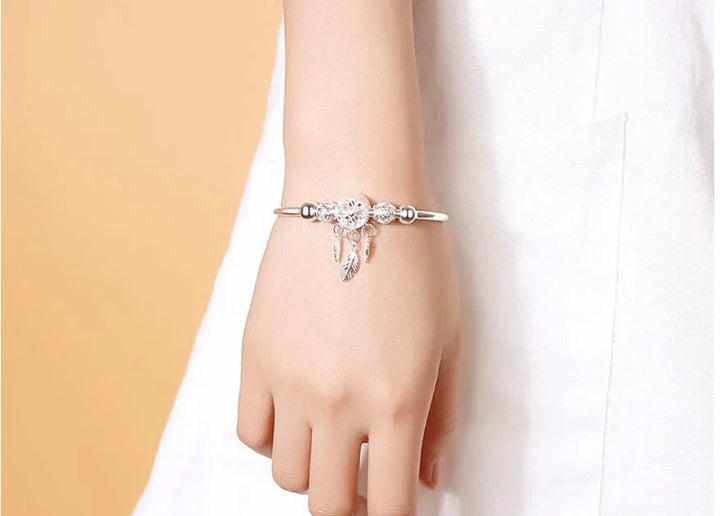 Silberarmband mit Anhängern an weiblichem Handgelenk, elegantes Schmuckdesign.