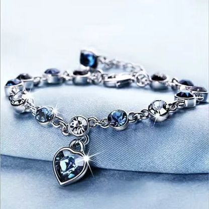 Silberarmband mit blauen Kristallen und Herzanhänger, funkelnd, elegantes Schmuckdesign.