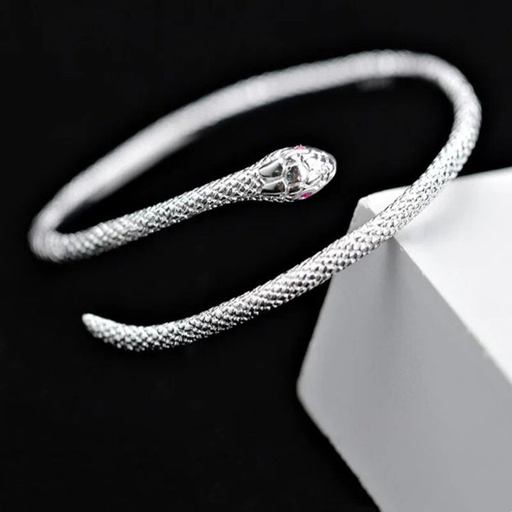 Silbernes Schlangenarmband, offenes Design, strukturiert, eleganter Schmuck auf schwarzem Hintergrund.