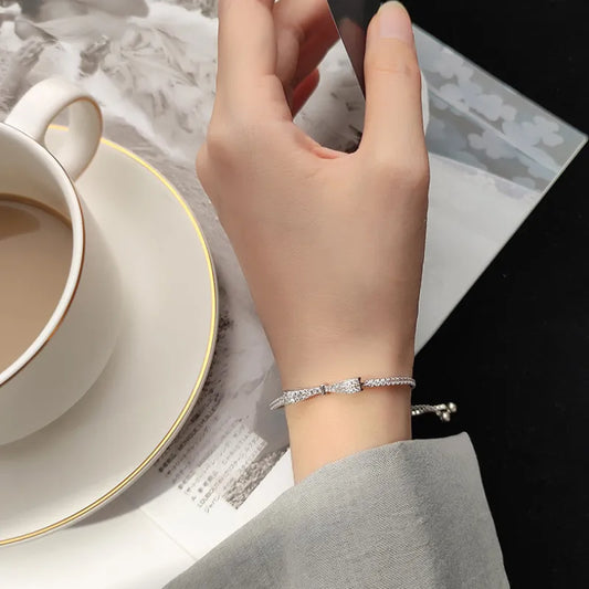 Silbernes Armband mit Strasssteinen an Hand, neben Kaffeetasse und Zeitschrift.