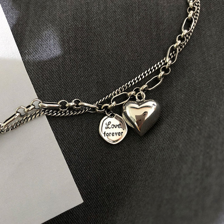 Silberarmband mit Herzanhänger und "Love forever"-Gravur auf grauem Hintergrund.