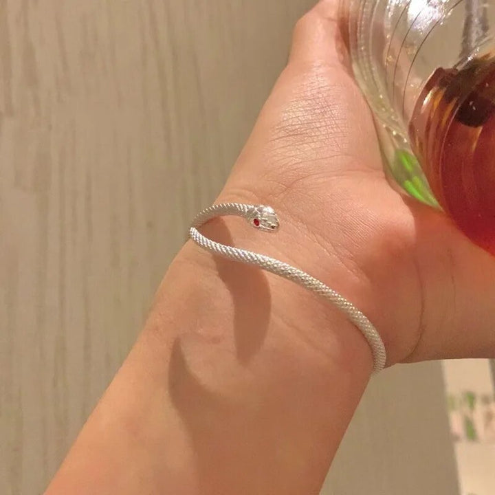 Silbernes Schlangenarmband mit rotem Auge auf Handgelenk, eleganter Schmuck, modisch.