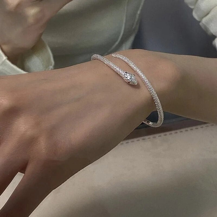 Silbernes Schlangenarmband mit Kristallkopf auf Handgelenk, eleganter Schmuck, modisch.