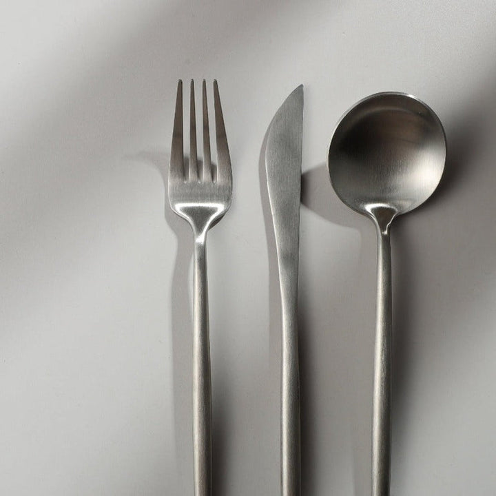 Minimalistisches Besteckset aus Edelstahl, bestehend aus Gabel, Messer und Löffel auf weißem Hintergrund.