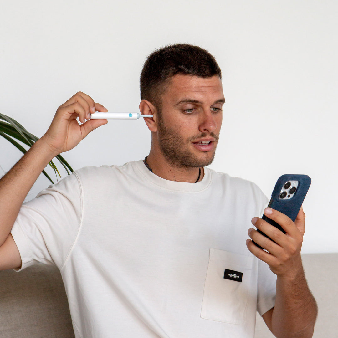 Mann mit Smartphone und Ohrreiniger, weißes T-Shirt, moderne Technologie, Hygieneprodukt.