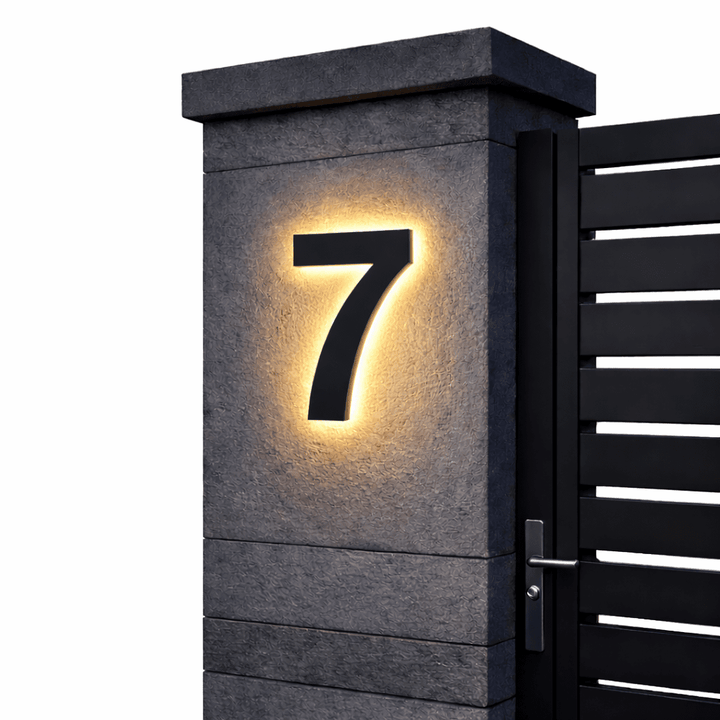 Černá podsvícená číslice 7 na tmavém kamenném sloupku vedle černé lamelové branky, bílé pozadí. 13