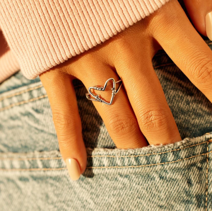 Silberner Herzring an Hand, Damenmode, Jeans, Strickpullover, Schmuckaccessoire.
