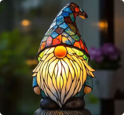 Svítící vitrážová lampa ve tvaru trpaslíka s modrou mozaikovou čepicí a zářící bílou bradou, v zahradním prostředí. 13