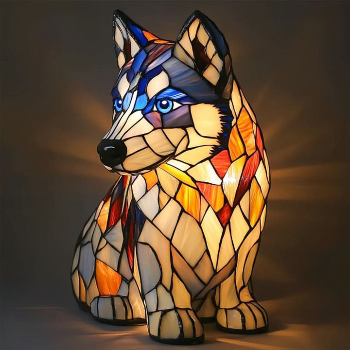 Sedící lampa ve tvaru huskyho s modrýma očima a krémovo-oranžovým vitrážovým tělem, svítící na tmavém pozadí. 15