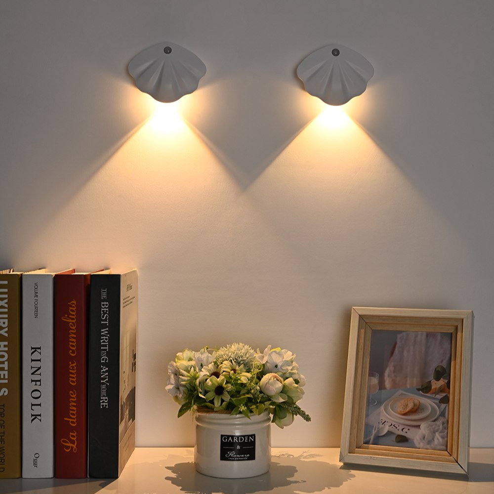 Zwei Muschel-Wandleuchten, warmes Licht, Bücherregal, Blumenstrauß, gerahmtes Bild.