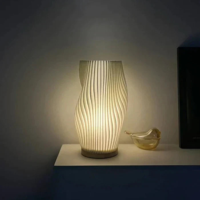 Moderne weiße Tischlampe mit wellenförmigem Design, leuchtend, auf einem Regal platziert.