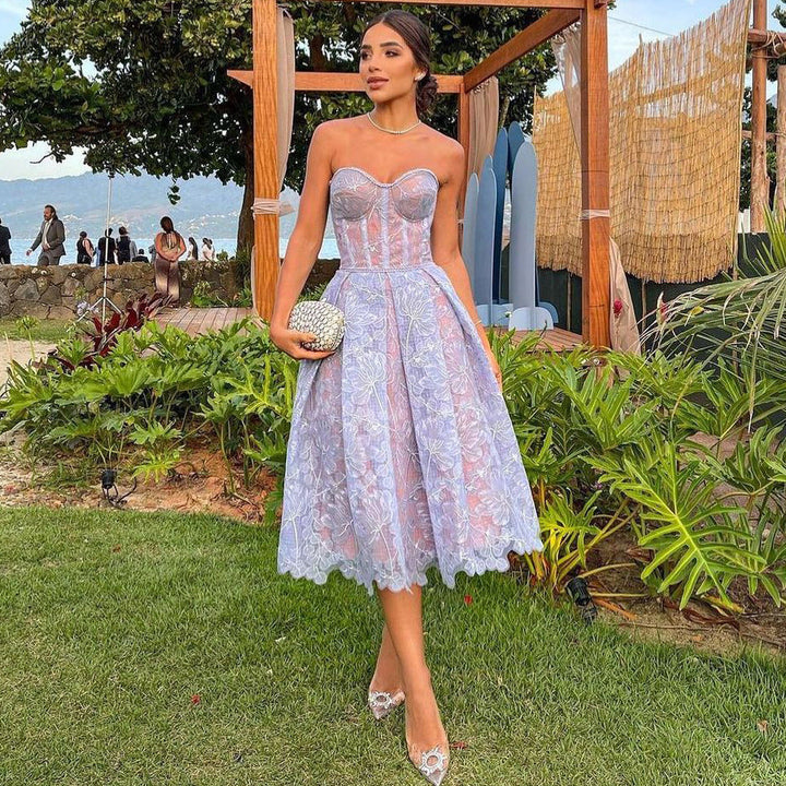 Frau in lila Spitzenkleid, trägerlos, mit Clutch, im Garten, elegantes Abendoutfit.