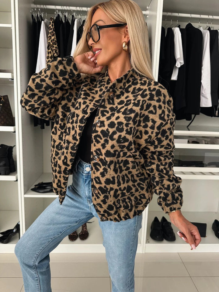 Modelka v bundě s leopardím vzorem a knoflíky, černý top a džíny, poloprofil a ruka u obličeje v šatně. 1