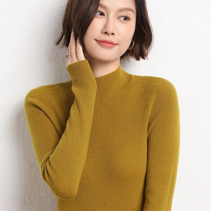 Frau in senfgelbem Strickpullover, lächelnd, vor weißer Wand.