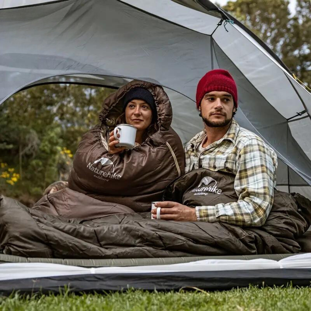 Zwei Camper in braunen Naturehike-Schlafsäcken im Zelt, trinken Kaffee, Outdoor-Abenteuer.