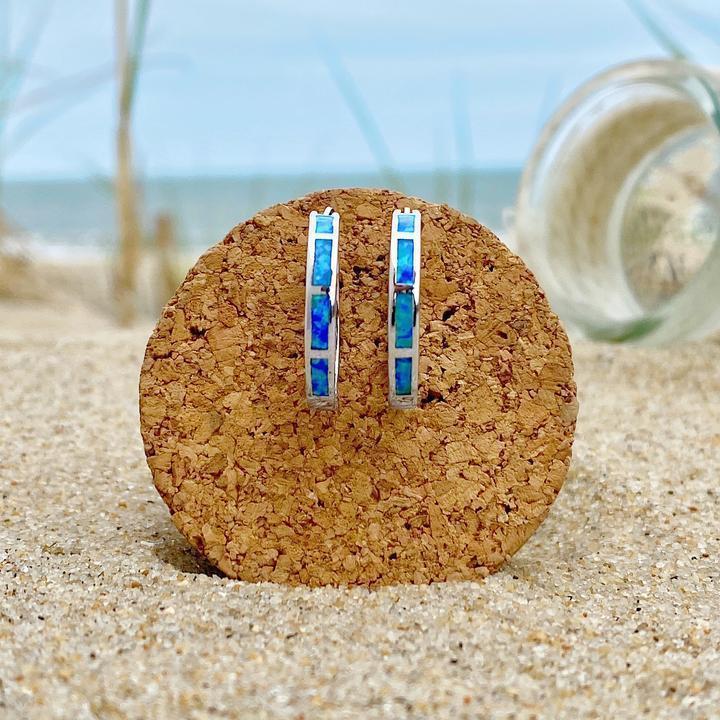 Blaue Opal-Creolen auf Kork, Strandhintergrund, eleganter Schmuck, maritimer Stil.