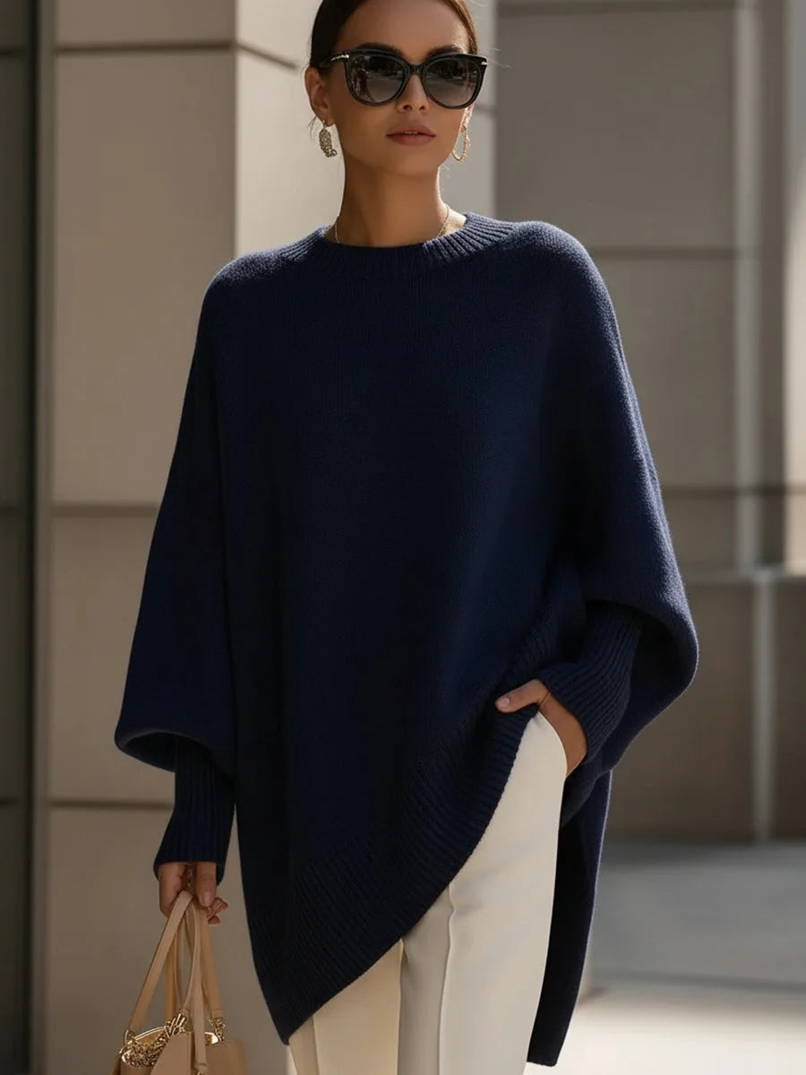 Tmavě modrý oversized svetr s asymetrickým lemem na modelce se sluneční brýlemi, ruka v kapse bílých kalhot. 8