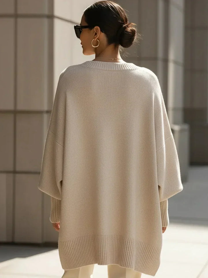 Béžový oversized svetr zezadu na modelce se sluneční brýlemi, drdolem a širokým žebrovaným lemem. 4