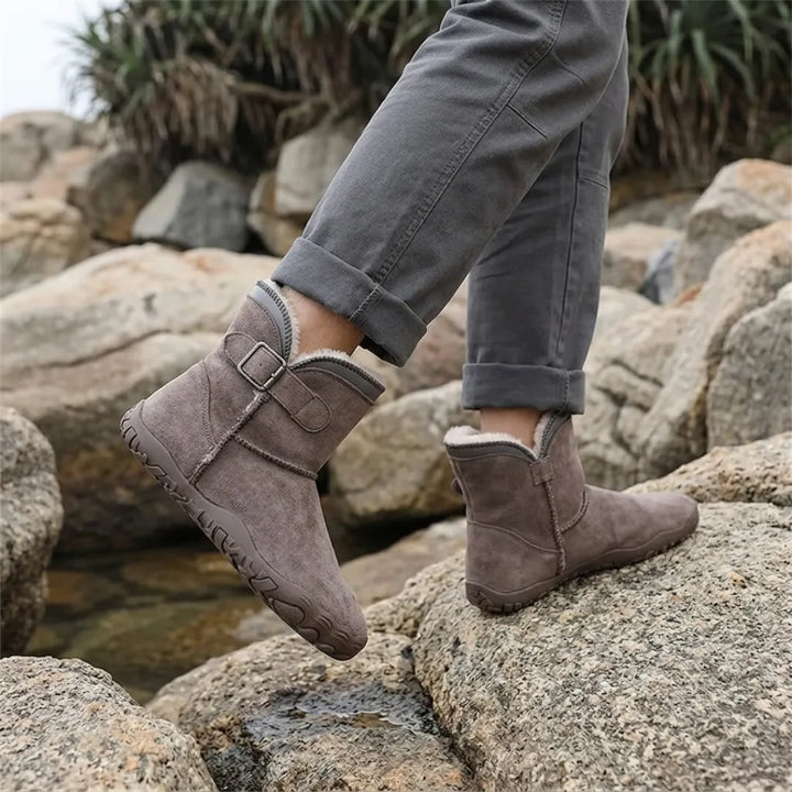 Šedohnědé semišové boty s huňatou podšívkou na nohou člověka stojícího na kamenech u vody 38