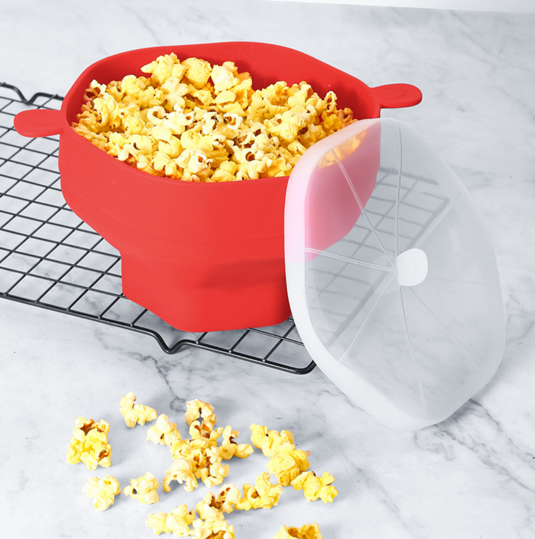 Roter Silikon-Popcorn-Maker mit Deckel auf Gitterrost, gefüllt mit frischem Popcorn.