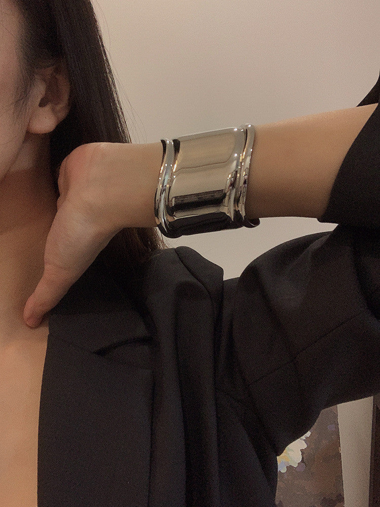 Silbernes, breites Metallarmband mit asymmetrischen Öffnungen, getragen am Handgelenk einer Frau.