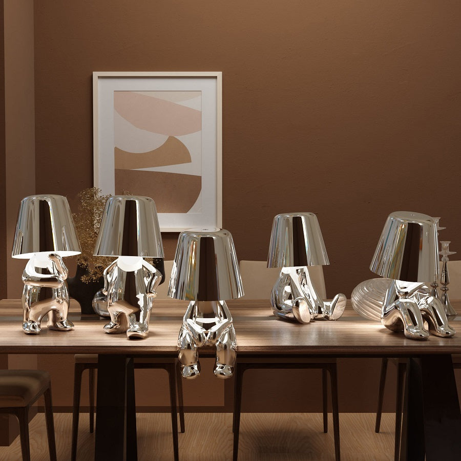 Vier silberne Designer-Tischlampen in Form von Figuren auf Holztisch, moderne Inneneinrichtung.
