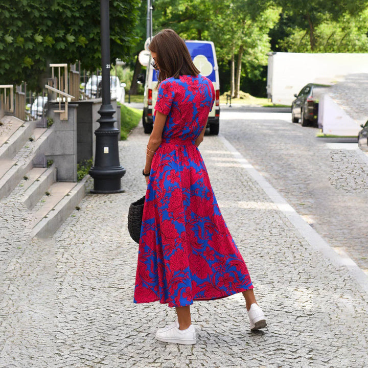Frau im rot-blauen Blumenkleid auf Kopfsteinpflasterstraße, Sommermode, Freizeitkleidung.