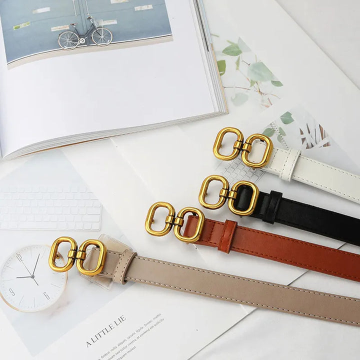 Vier Retro-Gürtel mit goldener Schnalle in Weiß, Schwarz, Braun und Beige auf einem Tisch.
