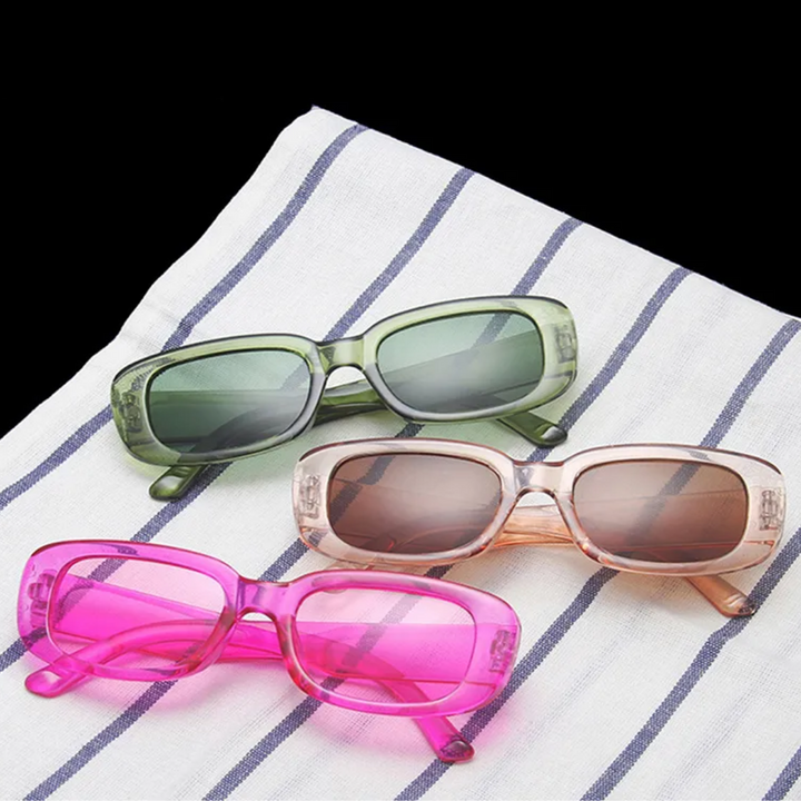 Drei Retro-Vintage-Sonnenbrillen in Grün, Rosa und Pink auf gestreiftem Tuch.