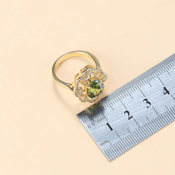 Goldener Ring mit grünem Edelstein und Zirkonia, neben Lineal zur Größenbestimmung.