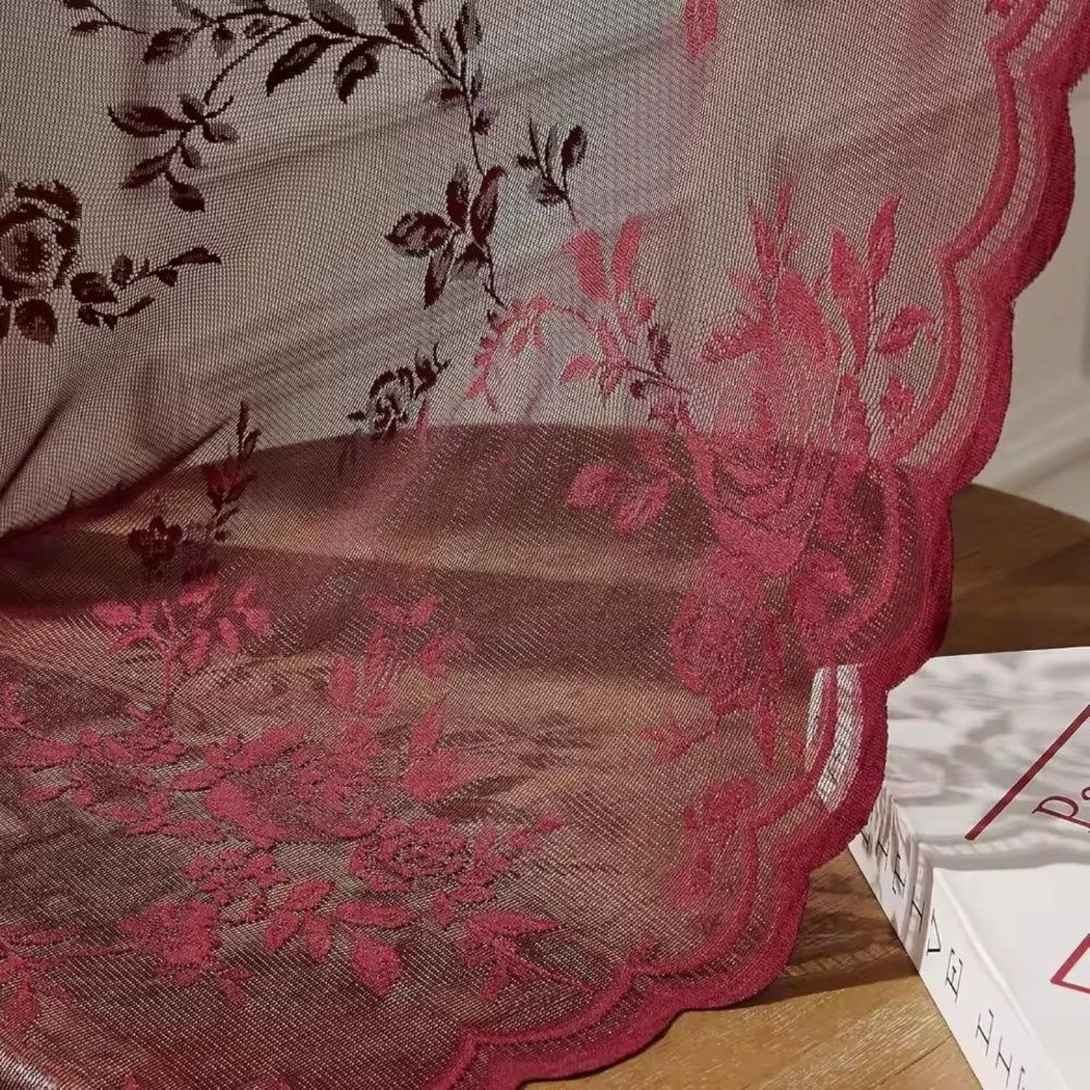 Detail vínově červené krajky s růžemi, jemnou síťovinou a vlnkovaným okrajem, položené na dřevěném povrchu. 3