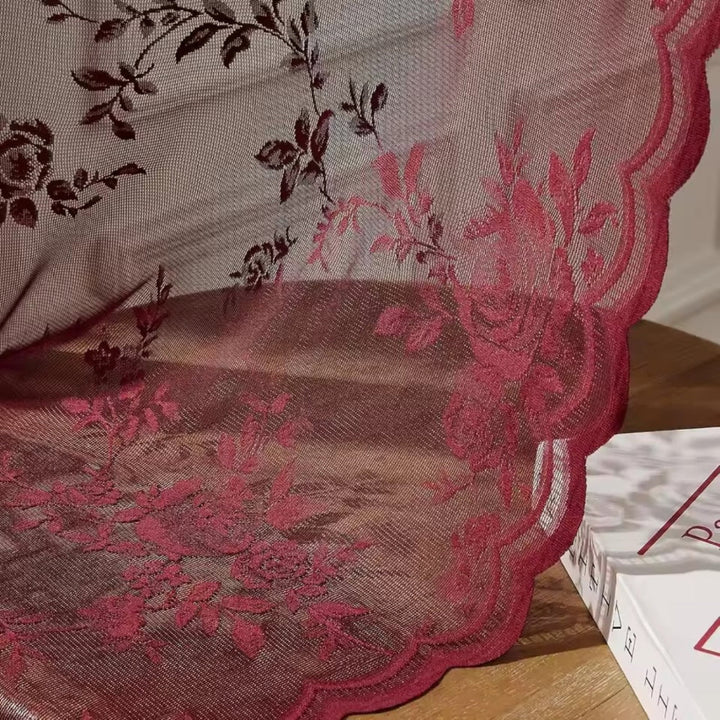 Detail vínově červené krajky s růžemi, jemnou síťovinou a vlnkovaným okrajem, položené na dřevěném povrchu. 3