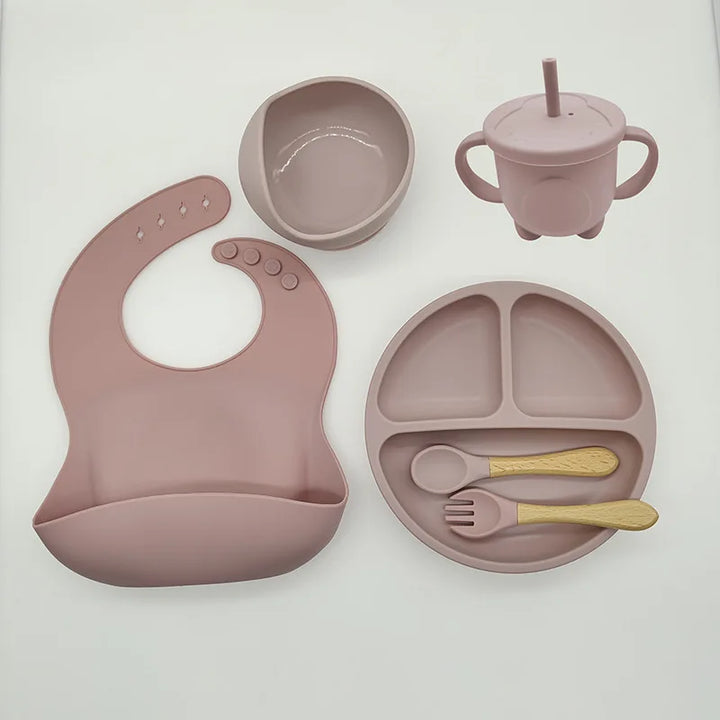 Rosa Silikon-Babygeschirr-Set mit Lätzchen, Teller, Schüssel, Becher, Löffel und Gabel.