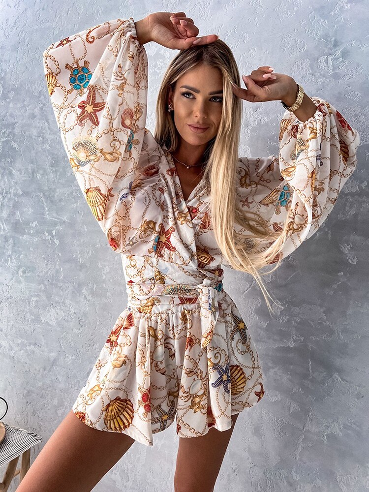 Frau in weißem, gemustertem Sommerkleid mit langen Ärmeln, lächelnd vor grauer Wand.