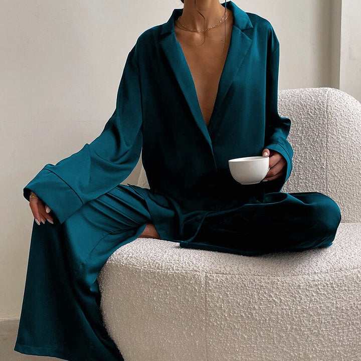 Frau in dunkelgrünem Satin-Pyjama mit Tasse, sitzt auf cremefarbenem Sofa.