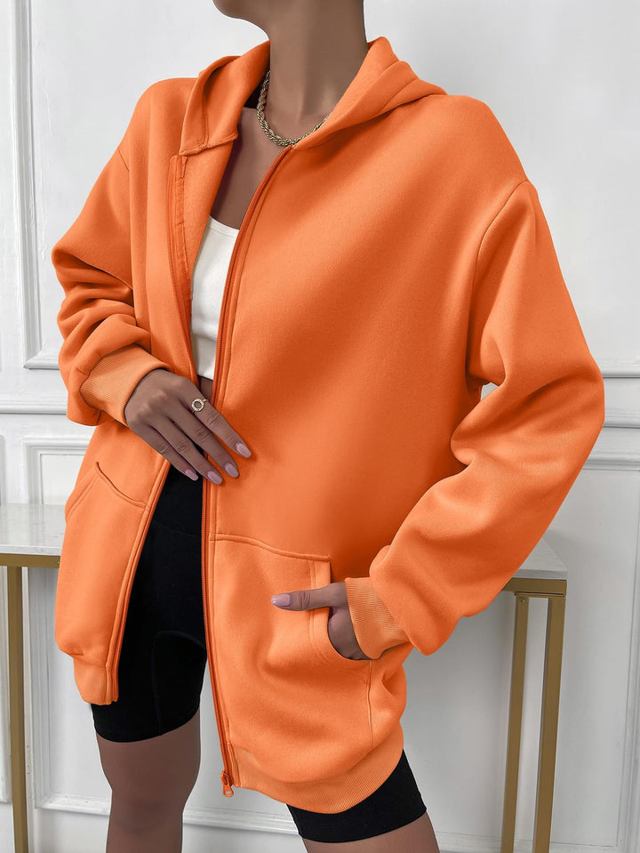 Frau trägt orange Kapuzenjacke, Reißverschluss, Taschen, modisch, lässig, bequem, Damenmode.