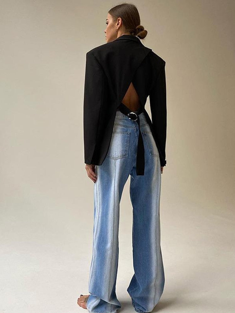 Frau in schwarzem Rückenfrei-Blazer und blauer Jeans, modisches Outfit, minimalistisch.