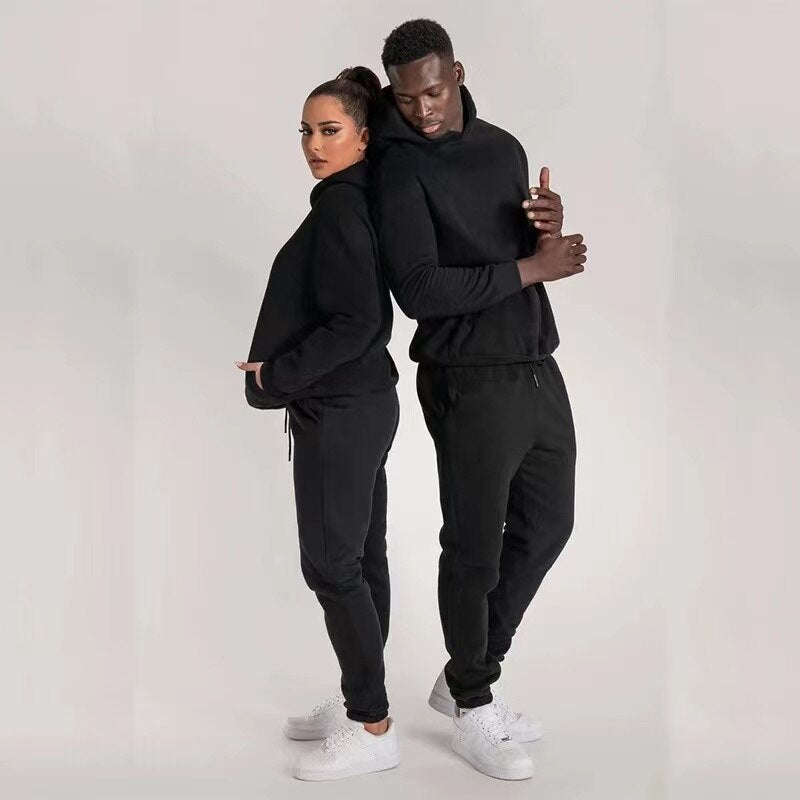 Zwei Personen in schwarzen Jogginganzügen, Hoodie und Jogginghose, weiße Sneaker, sportlich.
