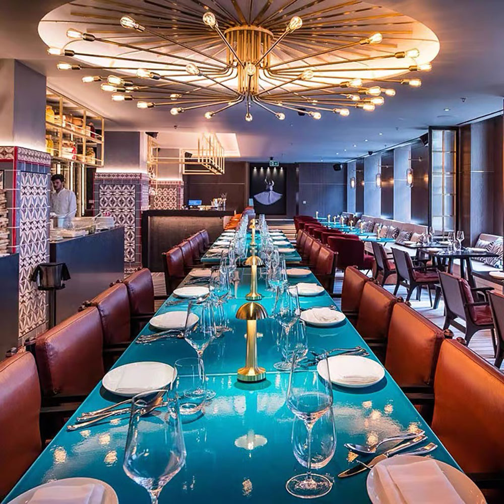 Elegantes Restaurant mit langem, türkisfarbenem Tisch, modernen Leuchten und gedeckten Plätzen.