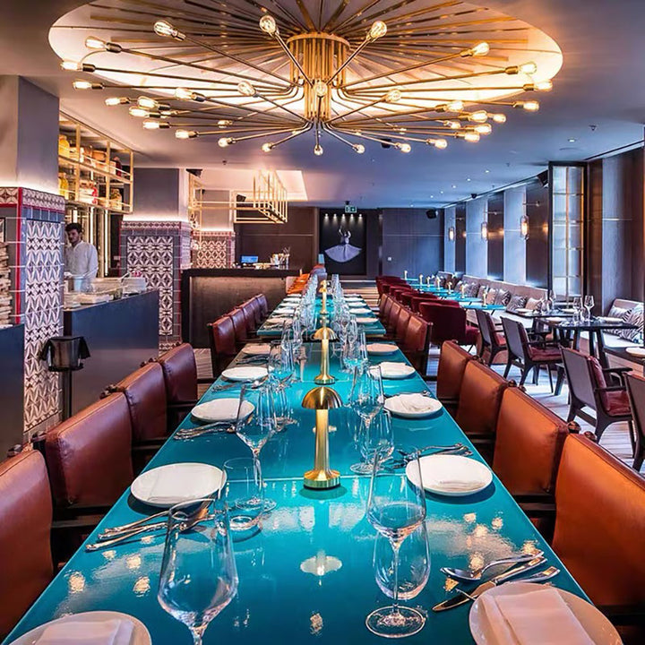 Elegantes Restaurant mit langem, türkisfarbenem Tisch, modernen Leuchten und gedeckten Plätzen.