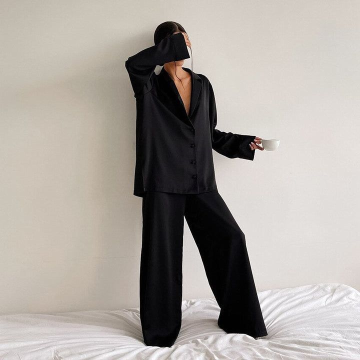 Frau in schwarzem Pyjama mit Kaffeetasse, minimalistisch, gemütliche Nachtwäsche, Schlafzimmer.