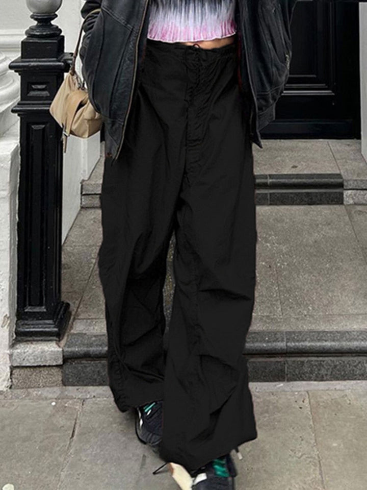 Frau in schwarzer, weiter Hose und Lederjacke auf Treppe, modischer Streetstyle-Look.