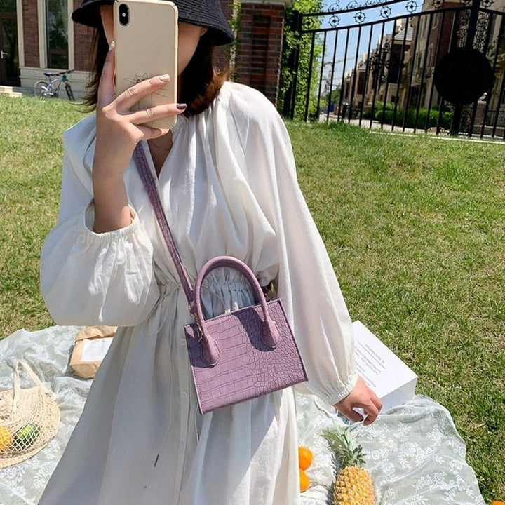 Frau mit weißem Kleid und lila Krokodilleder-Handtasche im Freien, Sommermode.