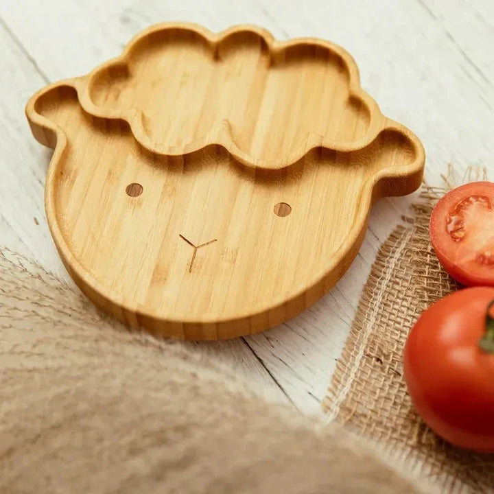 Bambus-Kinderteller in Schafform, umweltfreundlich, auf Holztisch mit Tomaten.