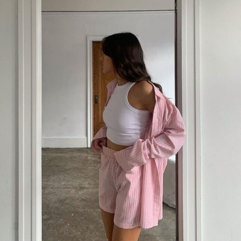 Frau in rosa gestreiftem Pyjama-Set und weißem Tanktop in minimalistischem Raum.
